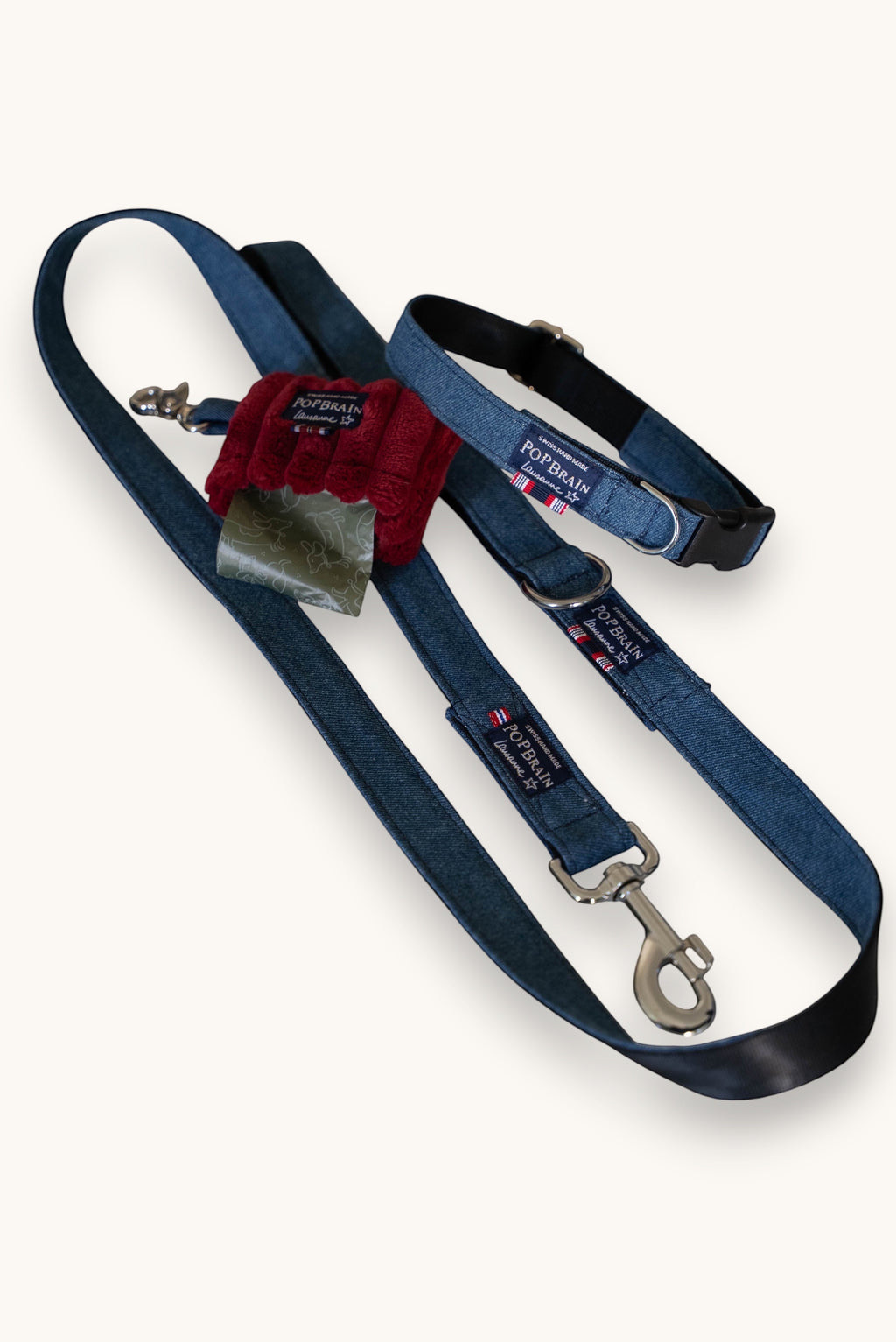 Popbrain indigo denim dog collar and leash set with silver hardware and a red waste bag dispenser on a white surface.